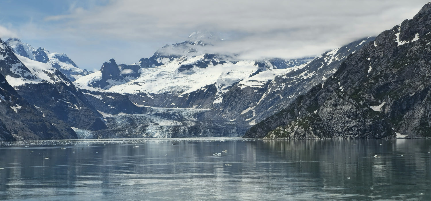 Snow-capped mountains and a tidewater glacier reflected in the calm water of an Alaskan fjord