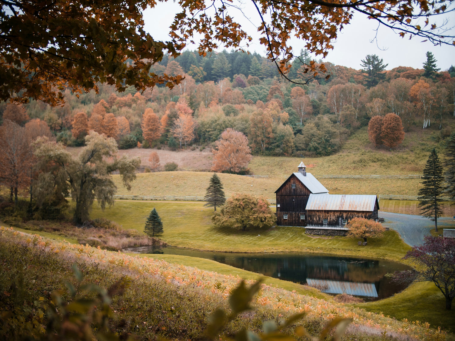 A red barn beside a pond surrounded by autumn foliage in Vermont