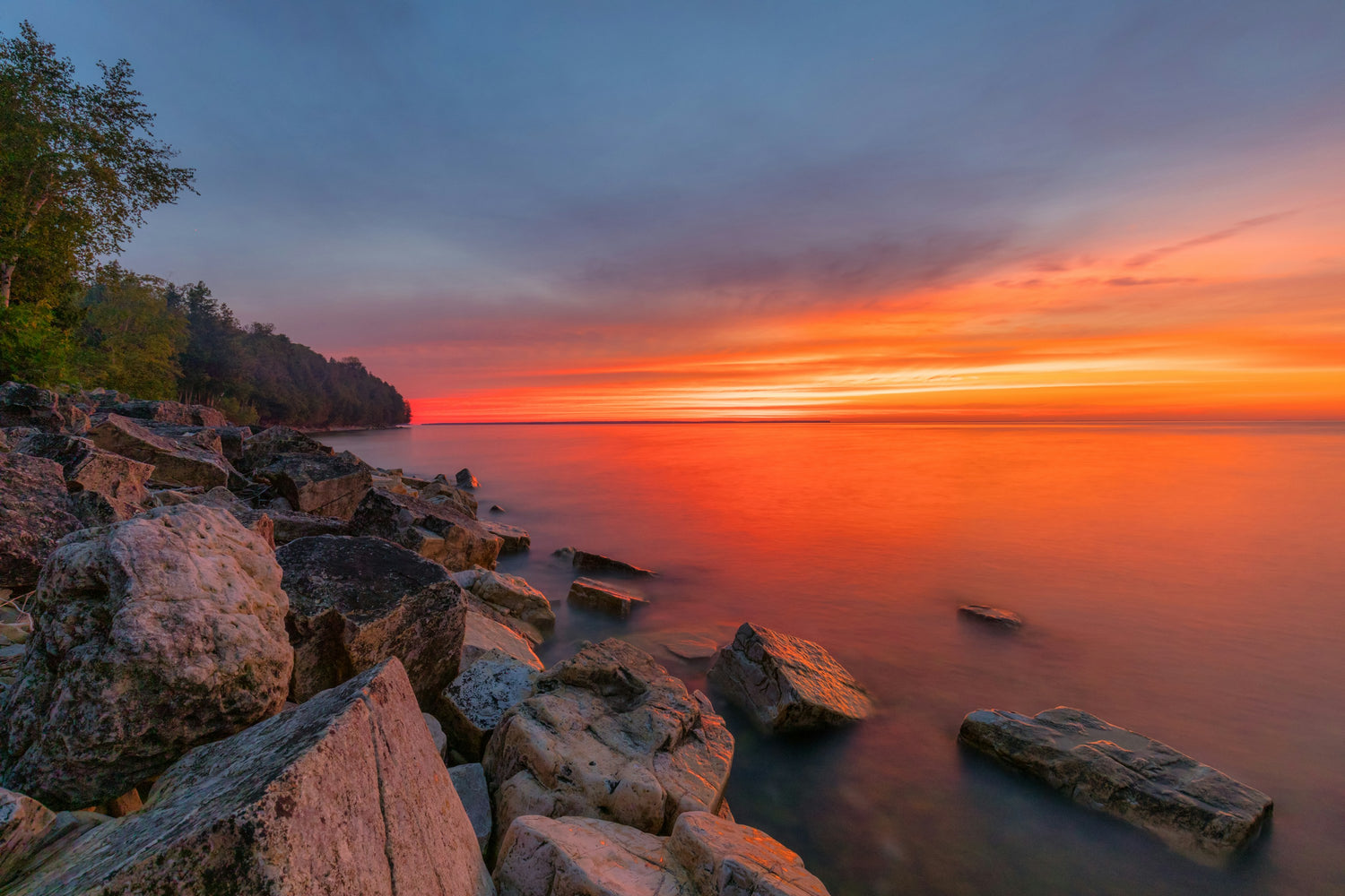 Sunset over the water with rocky shoreline in the foreground in Door County, Wisconsin